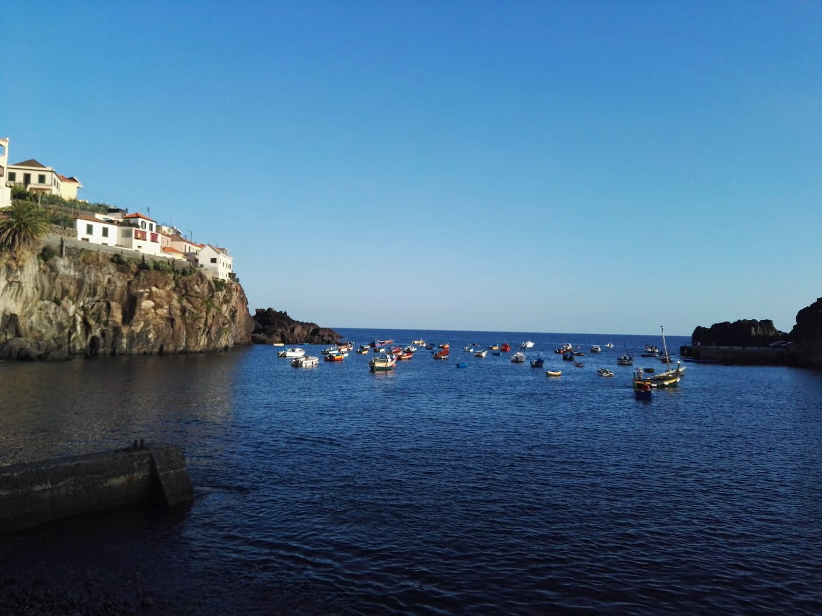 Small colourful fishing boats moored in the bay at Câmara de Lobos below a cliffside town