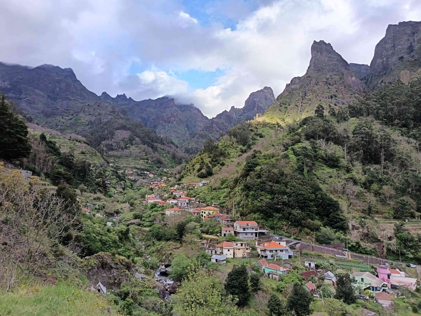 A village of red-roofed houses scattered across the floor of a deep green mountain valley, jagged peaks behind