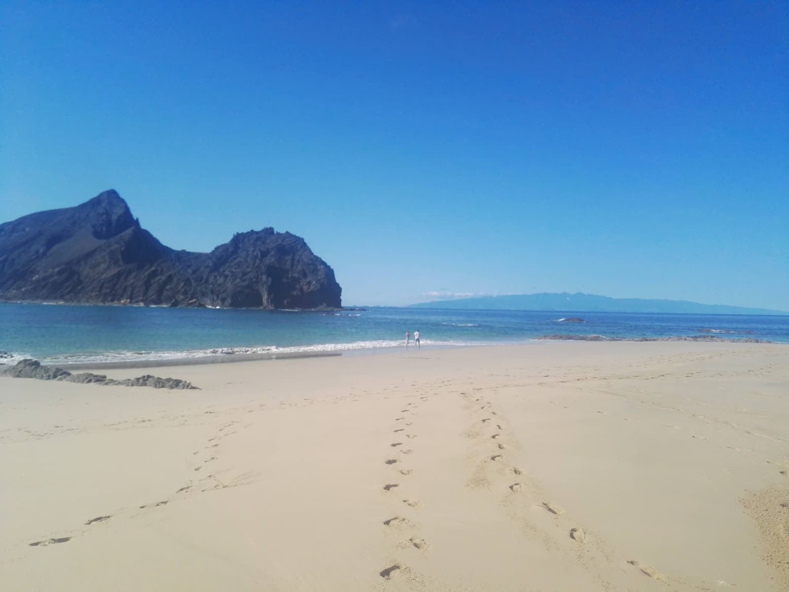 Footprints in coppery sand at Prainha beach with rocky cliffs behind