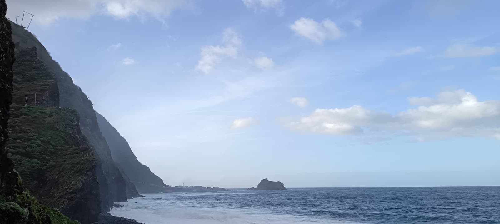 Green sea cliffs above the village of Ribeira da Janela with a sea stack islet offshore