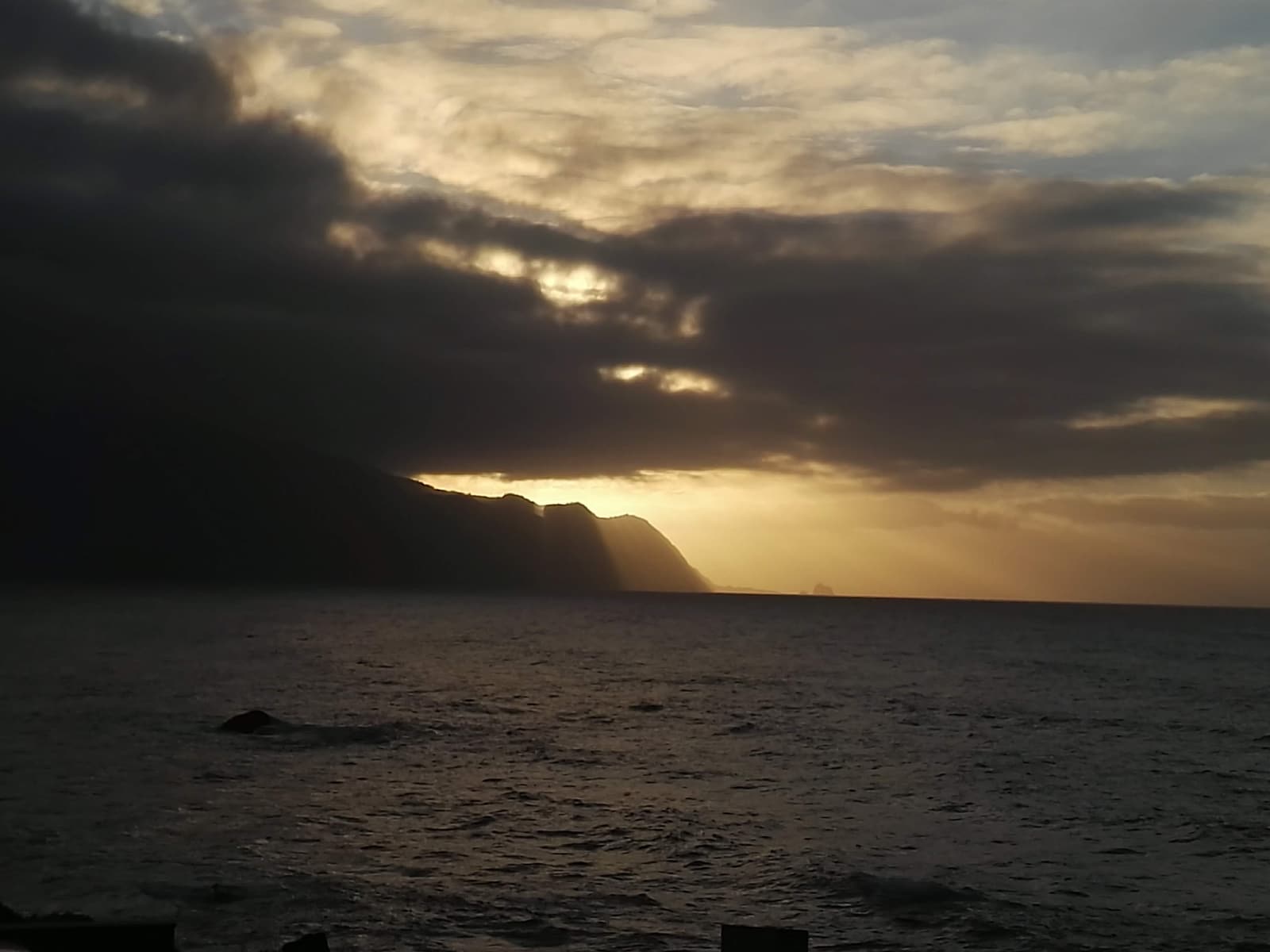 Tall green sea cliffs above Seixal lit by a low sunset sun with dramatic clouds